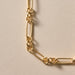 A close-up of a gold-toned chain necklace with elongated oval links and smaller connecting rings, laid on a warm off-white textured surface.