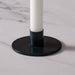 A close-up of a blue round candle holder base with a white candle inserted, set on a light marble surface.