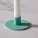 A close-up of a turquoise circular candle holder base, holding a white candle, set on a light marble surface.