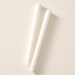 Two natural white colored pillar candles with ribbed bases, laying flat on a white background.