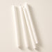 Four white taper candles, laying flat on a light beige background.