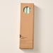 A tall, narrow cardboard box with a circular window display cutout at the top showing two sage green candles inside, photographed on a clean off-white background. The box has printed text near the bottom including the brand name 'Ten Thousand Villages'.