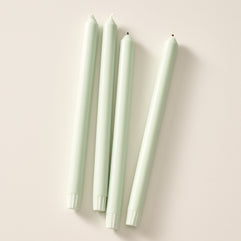 Four sage green taper candles laying flat on a light beige background.