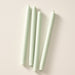 Four sage green taper candles laying flat on a light beige background.