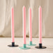 Four taper candles in a ginger color with turquoise and blue candle holder bases, arranged on a light surface against a soft beige fabric backdrop.