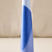 A close-up of a tapered candle with a blue and light blue geometric pattern, set against a neutral beige fabric background.