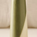 A close-up of a tapered candle with a vertical geometric design in olive green and cream, set against a soft beige background.