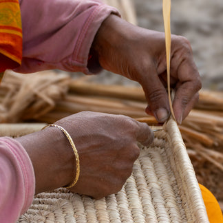 Close-up of a person's hands carving a brown clay pot with a wooden chisel, showing detailed hand tools and textures.
